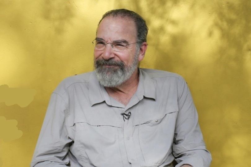  Portrait of Mandy Patinkin in front of a yellow-gold background. 