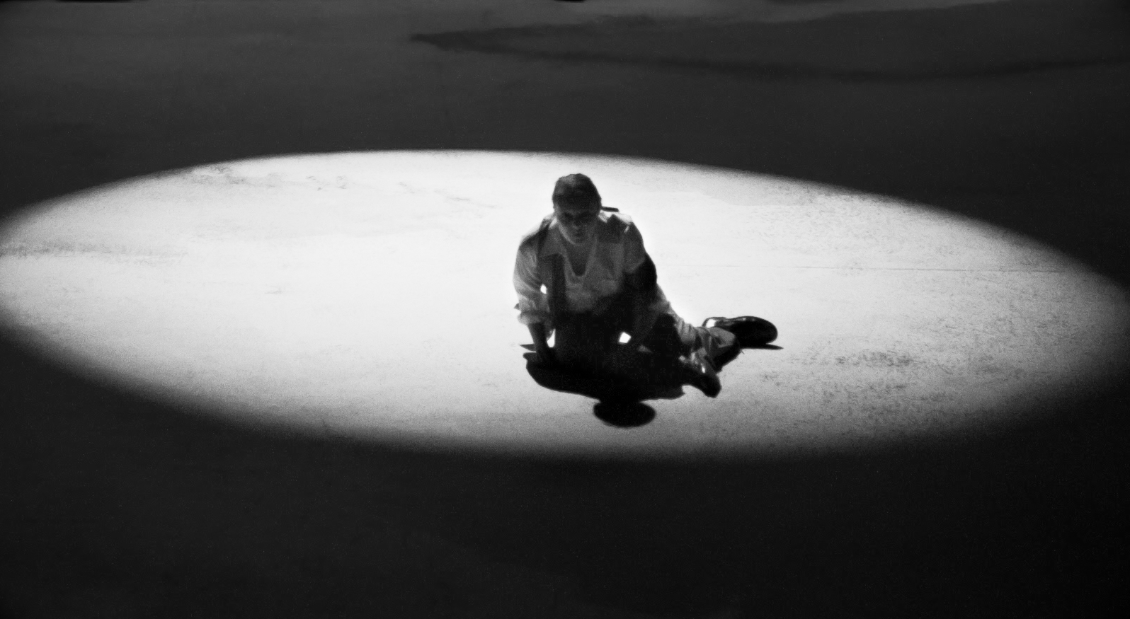 S.T. is shown as a well-dressed young man crumpled in a spotlight on the floor.  He looks disheveled.