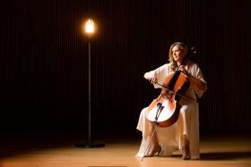 Portrait of cellist on a dark stage in a pool of gold light.