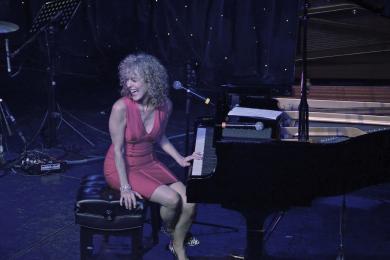 Portrait of Judy Carmichael sitting at a grand piano. 