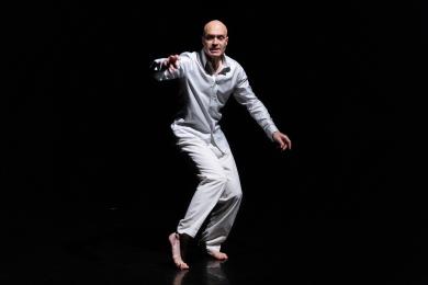 A bald man in an all white outfit on a dark black background