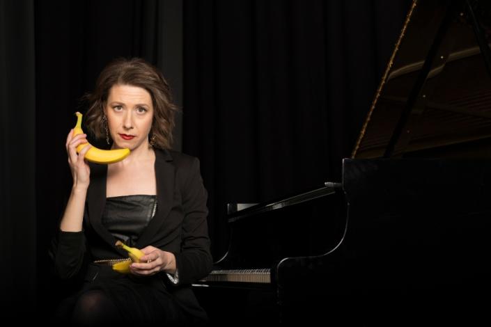 Sarah Hagen holding a banana phone on a dark background. 