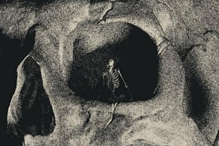 Skeleton standing in the eye of a giant skull.