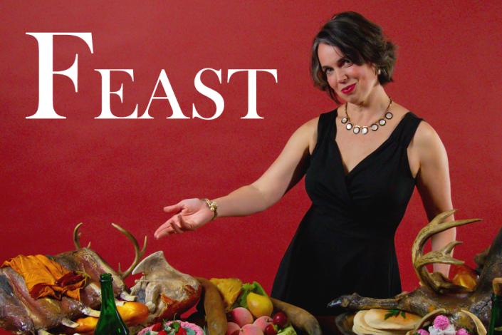 An elegant woman gestures in invitation towards a table absolutely loaded with food, everything from pretty cakes to haunches of meat.