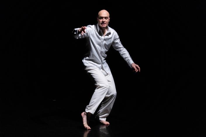 A bald man in an all white outfit on a dark black background