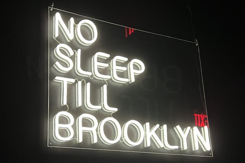 An old fluorescent sign in white says "No Sleep Till Brooklyn"